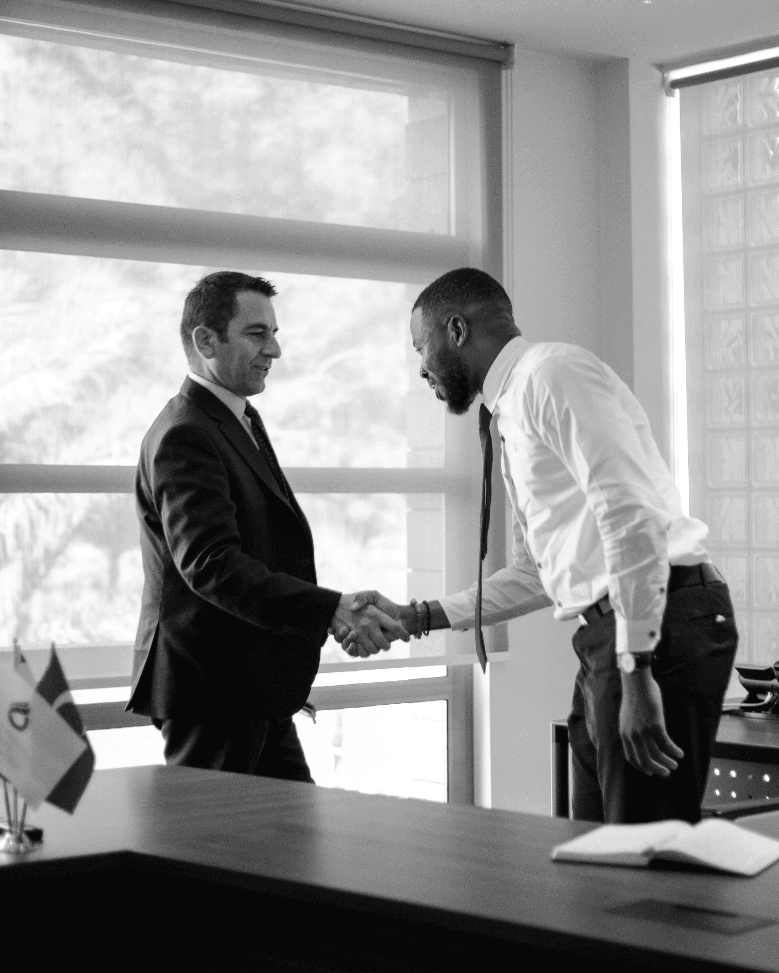Two businessmen shaking hands across a desk.