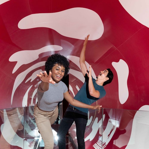 Due persone che posano in modo giocoso all'interno di un tunnel rosso e bianco con motivi dinamici sulle pareti.
