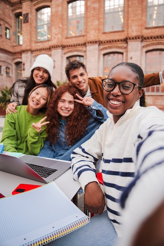 Smiling group of diverse students taking a selfie outdoors.