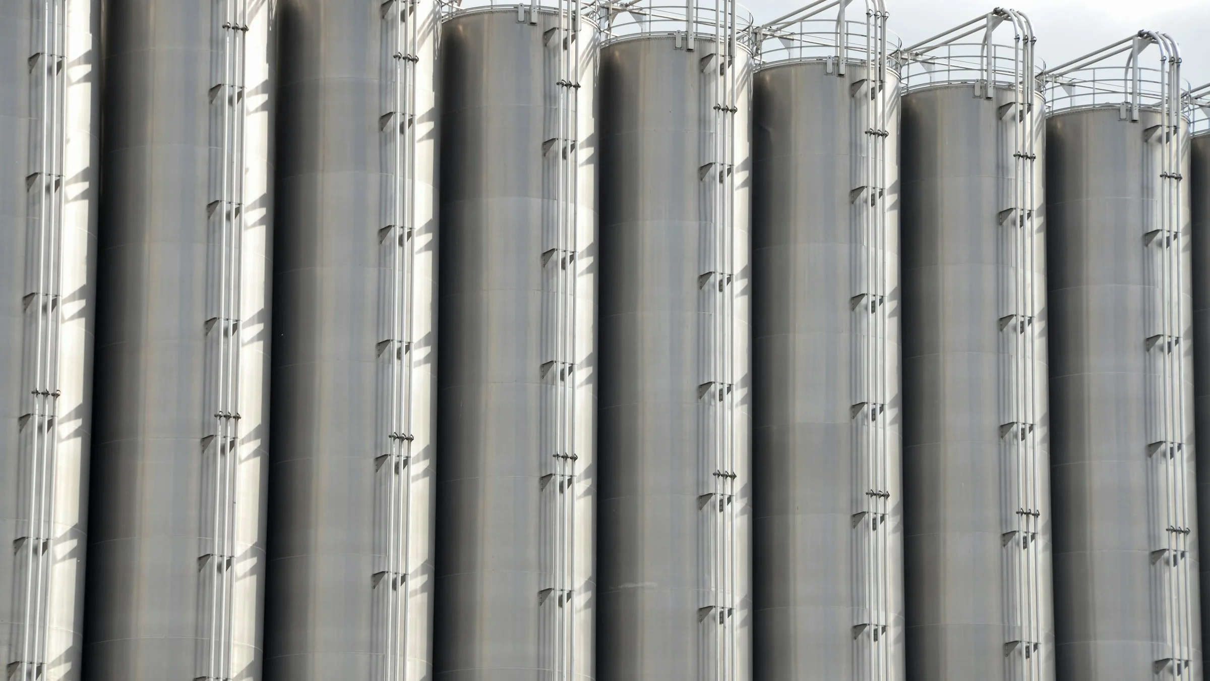 A row of tall stainless steel storage vessels at an industrial site