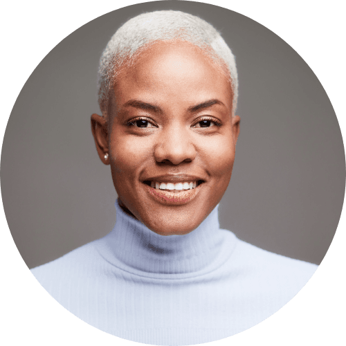 Portrait of a smiling woman with short gray hair, wearing a white turtleneck, with a gray background.