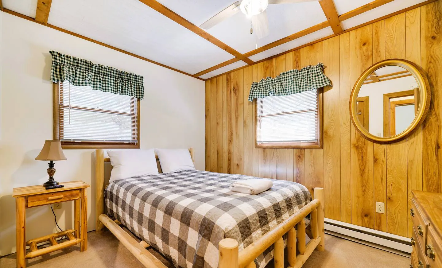 Queen log bed with checked quilt and round mirror on pine wall at RedHawk Chalet