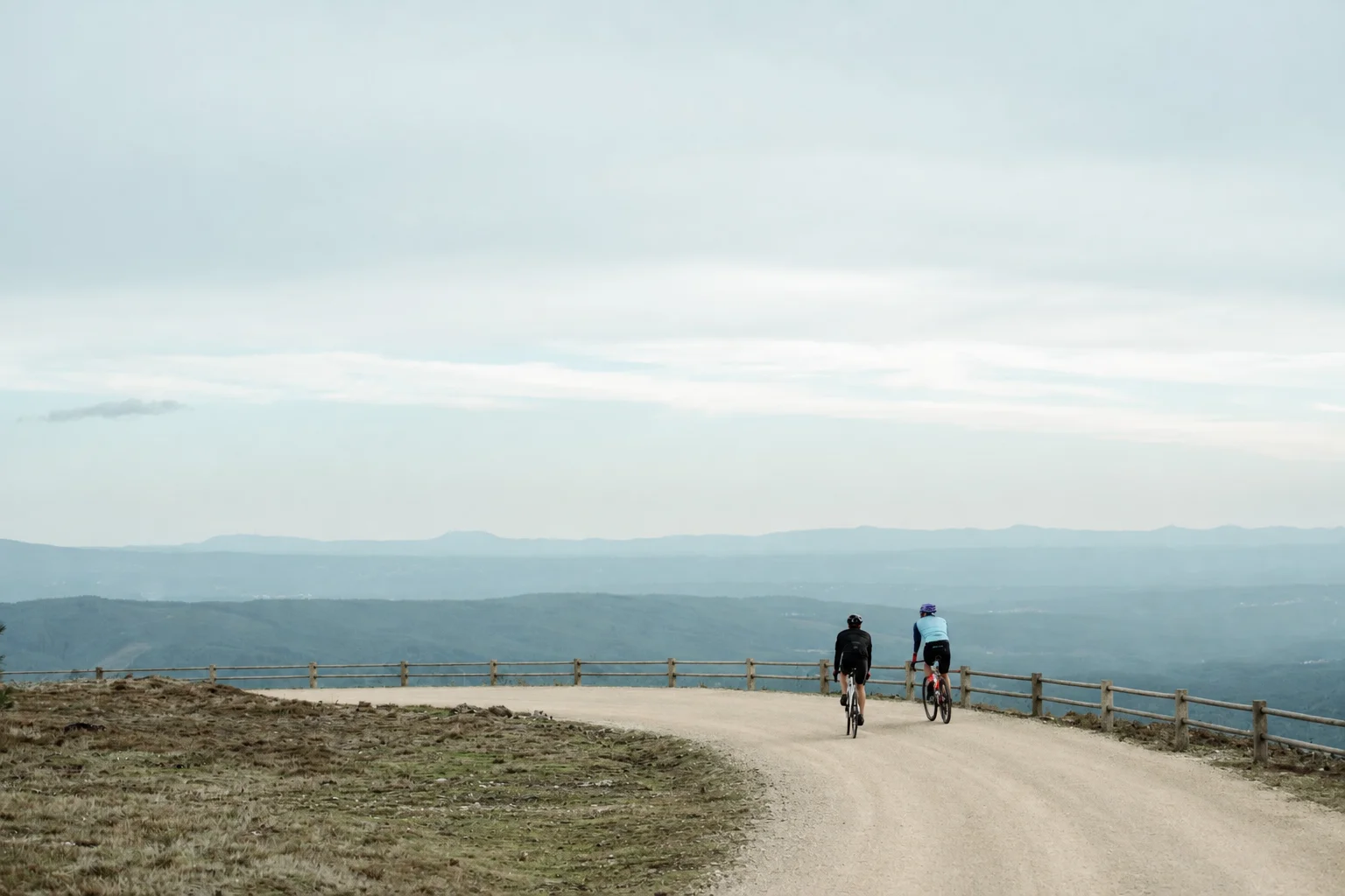 two people riding their bike on a gravel road
