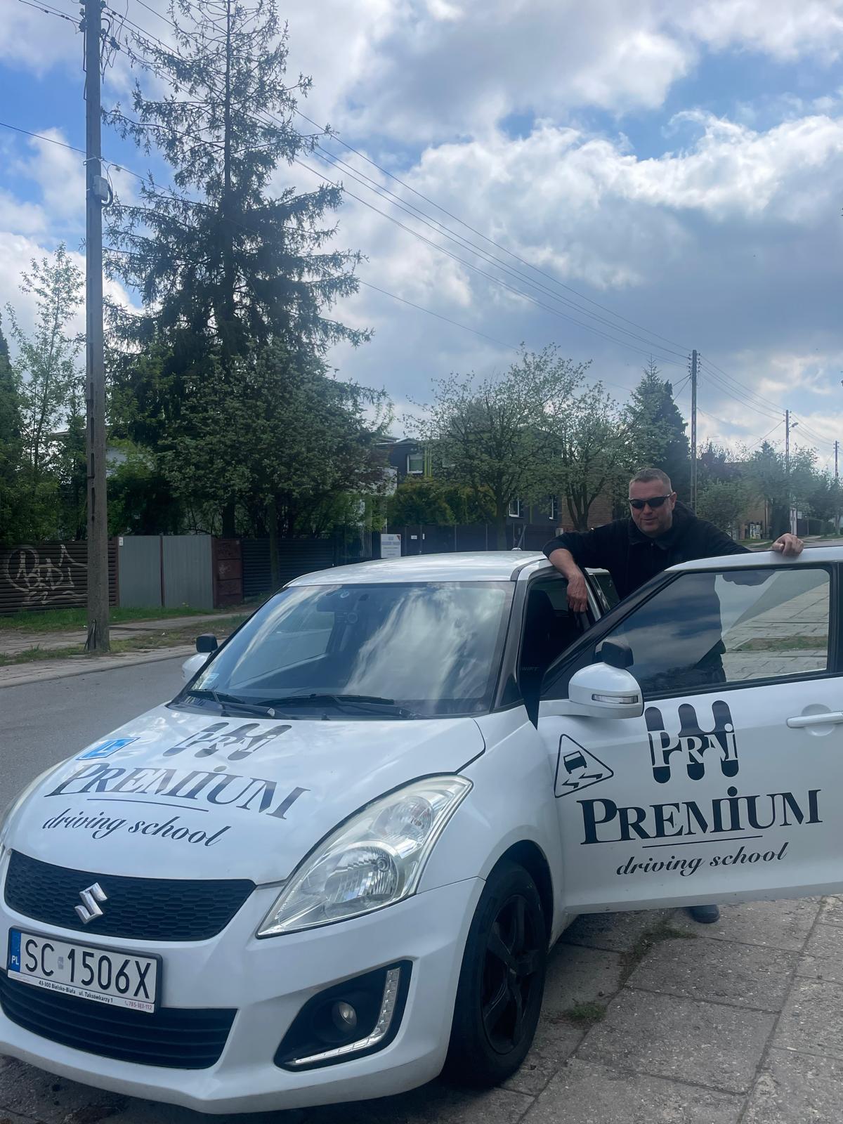 Artur Jundzill – Instruktor opierający się o biały samochód nauki jazdy Premium.