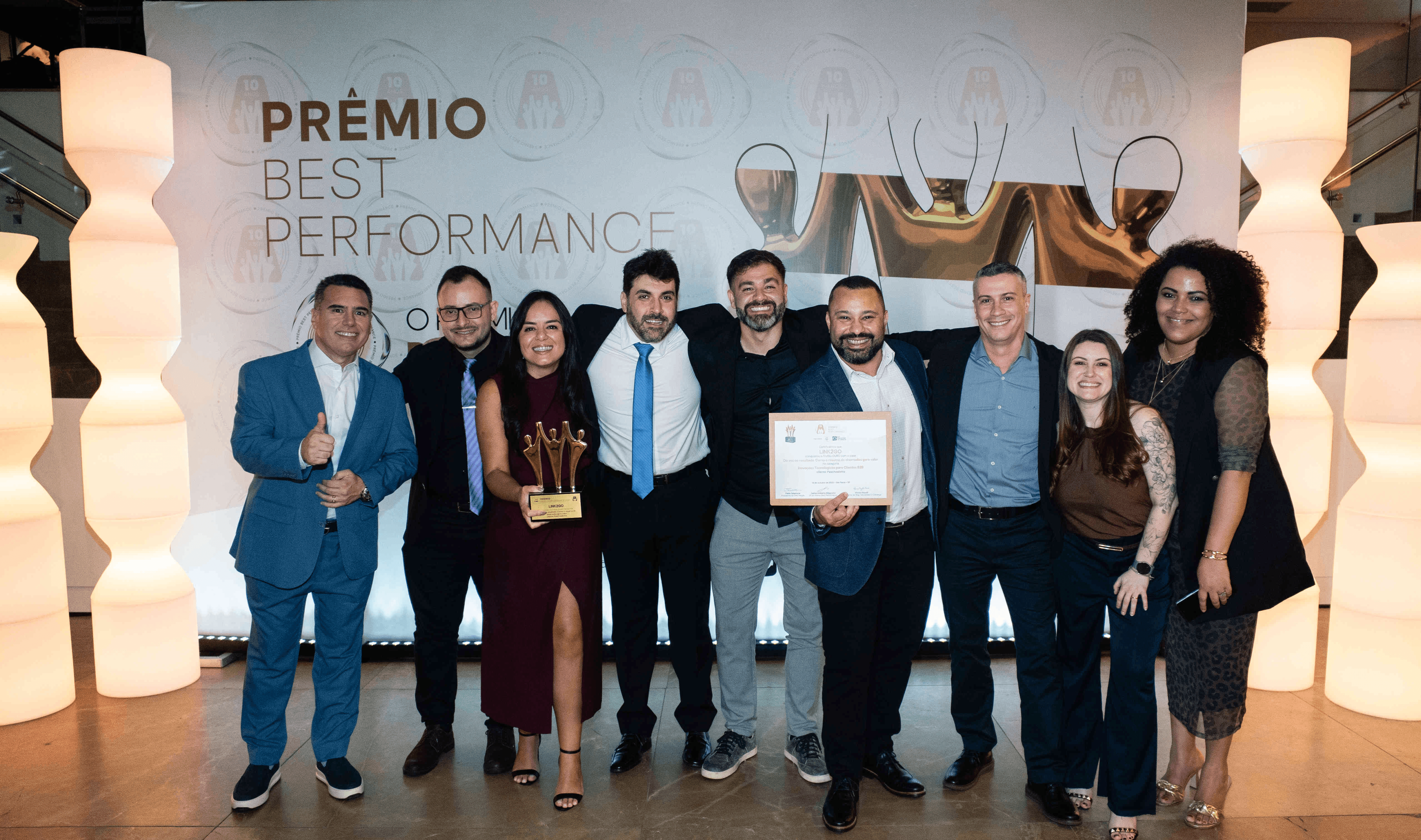 Executivos da LINK2GO posando com troféu ouro e certificado no palco do Prêmio Best Performance 2025