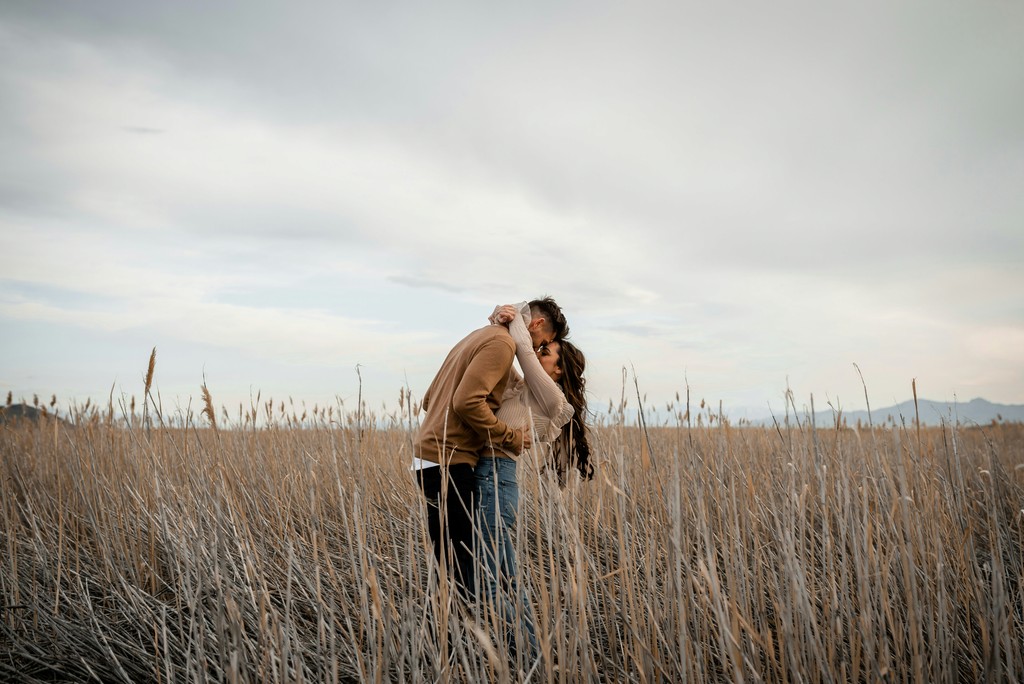 Couple embracing in a golden dried grass field under an overcast sky with distant mountains on the horizon