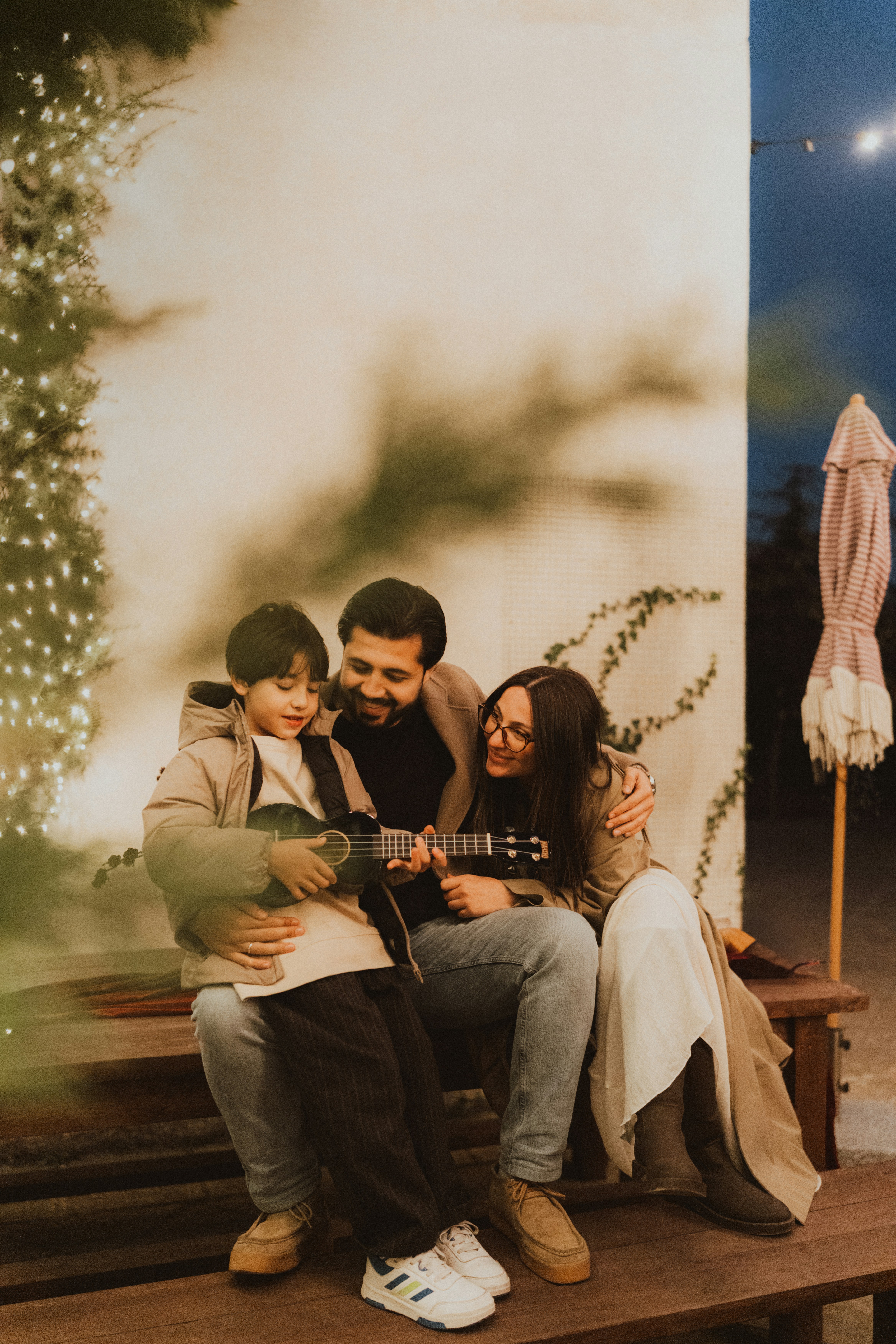Family playing ukulele on a bench outdoors