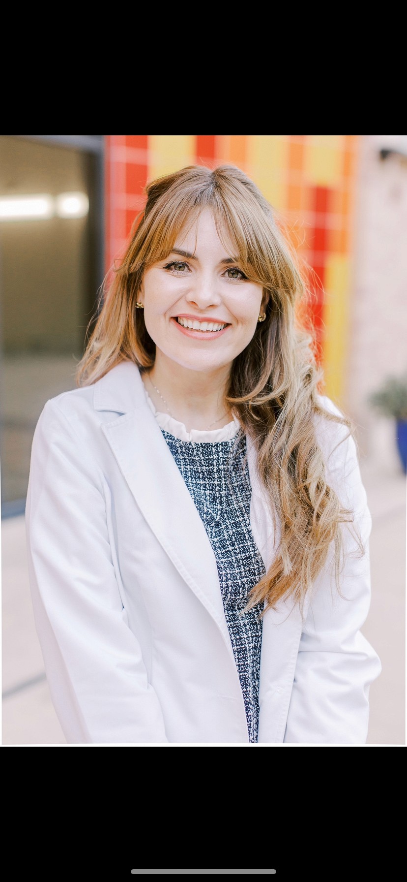 Gabriela Fabricio in a white coat in front of an orange geometric wall