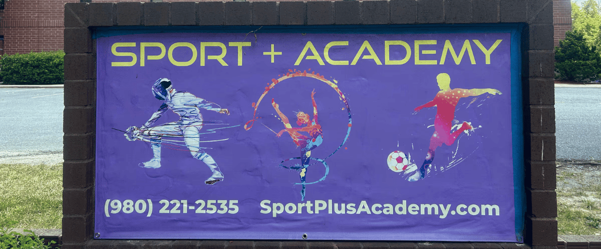 The monument business sign that stands in front of the parking lot of SportPlus Academy's gym in Indian Trail, NC at 3016 Sardis Dr with some sports drawn on it and business name, phone number, and email printed