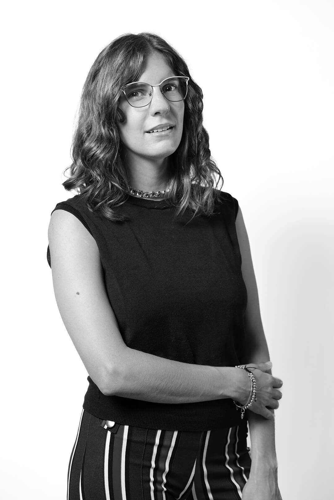 Black and white portrait of a woman with wavy hair, wearing glasses, a sleeveless top, and striped pants. She displays a calm and composed expression.