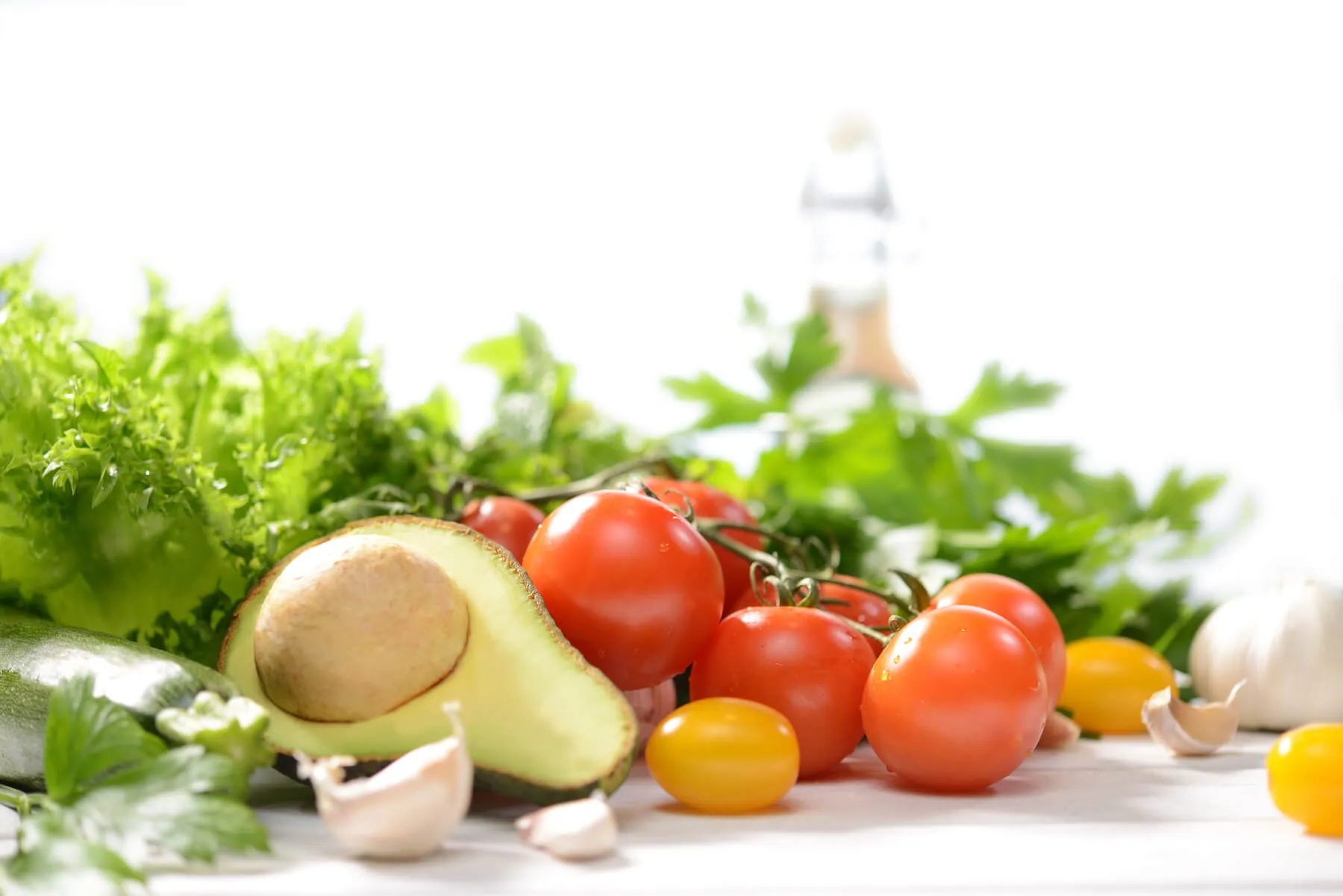 A colorful array of fresh vegetables including tomatoes, lettuce, and garlic on a white background.