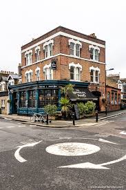 A smiling man with curly hair is sitting at a desk, looking at the camera, with a laptop and a lamp in the background.