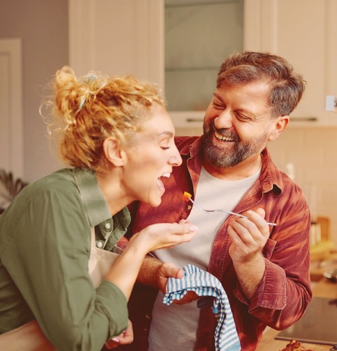 Married couple cooking together, taste testing the food.