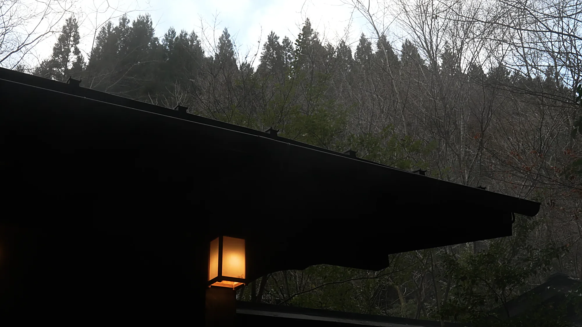 A dark eave at Kurokawa Onsen at dusk with a single glowing lantern