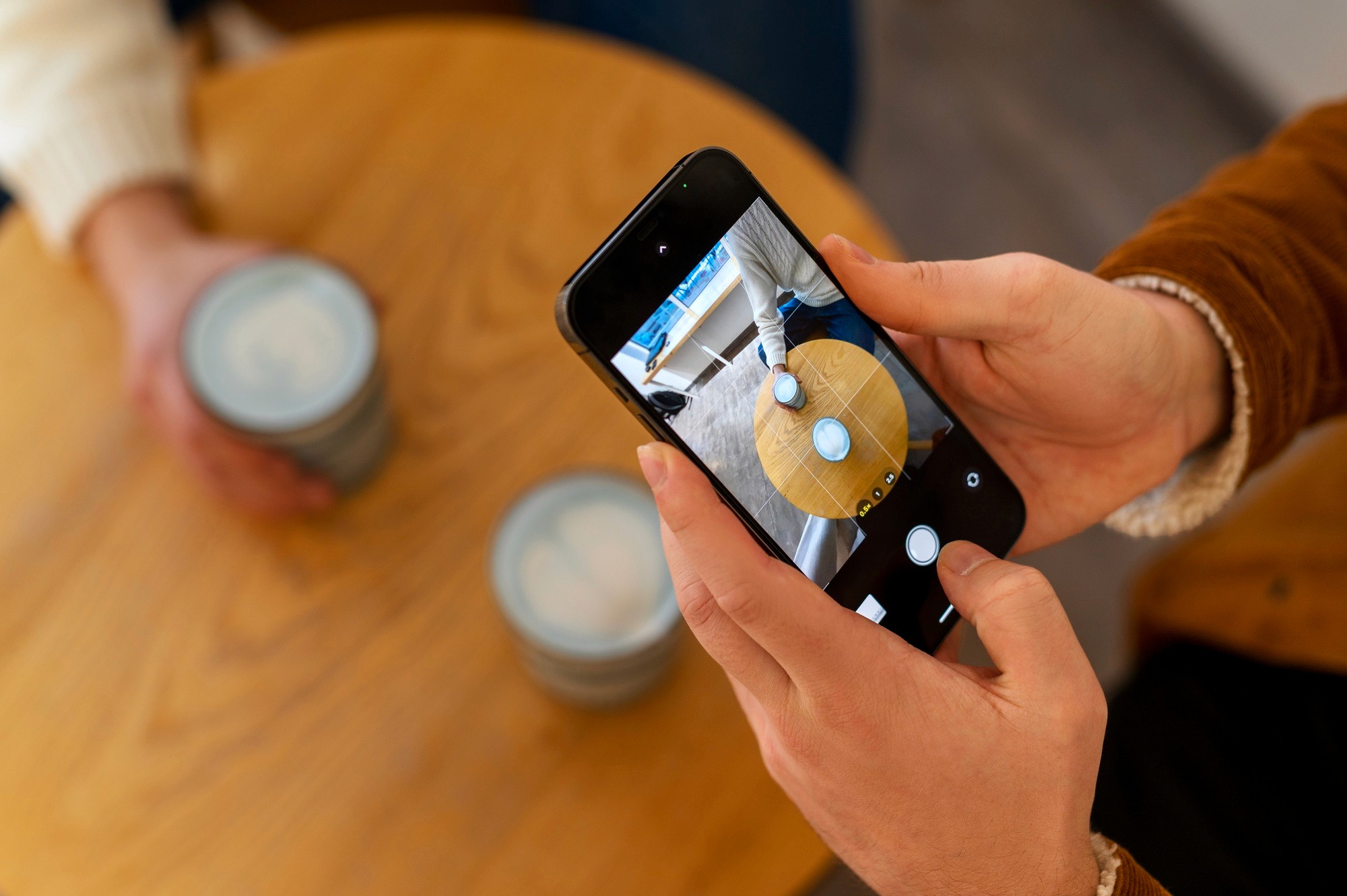 Person using a smartphone to photograph coffee cups on a wooden table