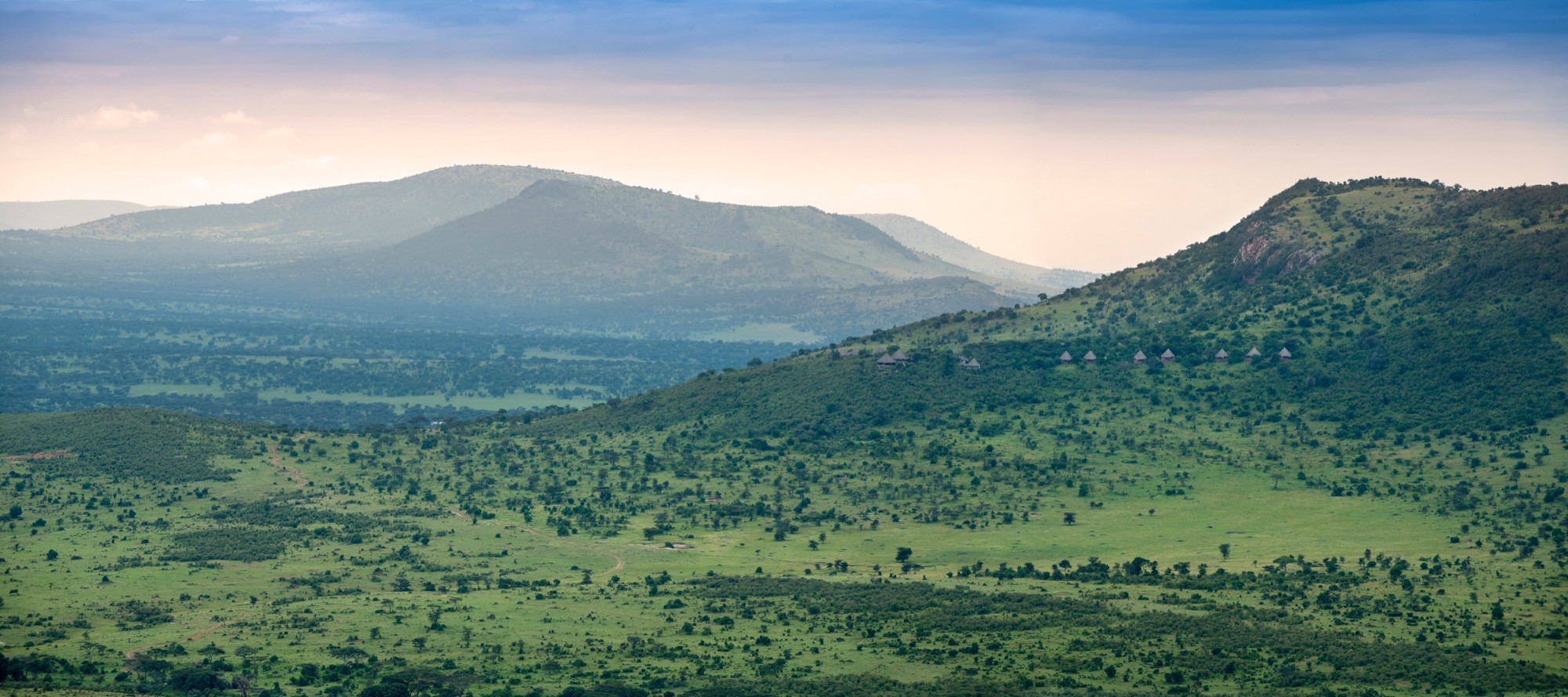 Green hills rolling toward distant ranges under a soft evening sky
