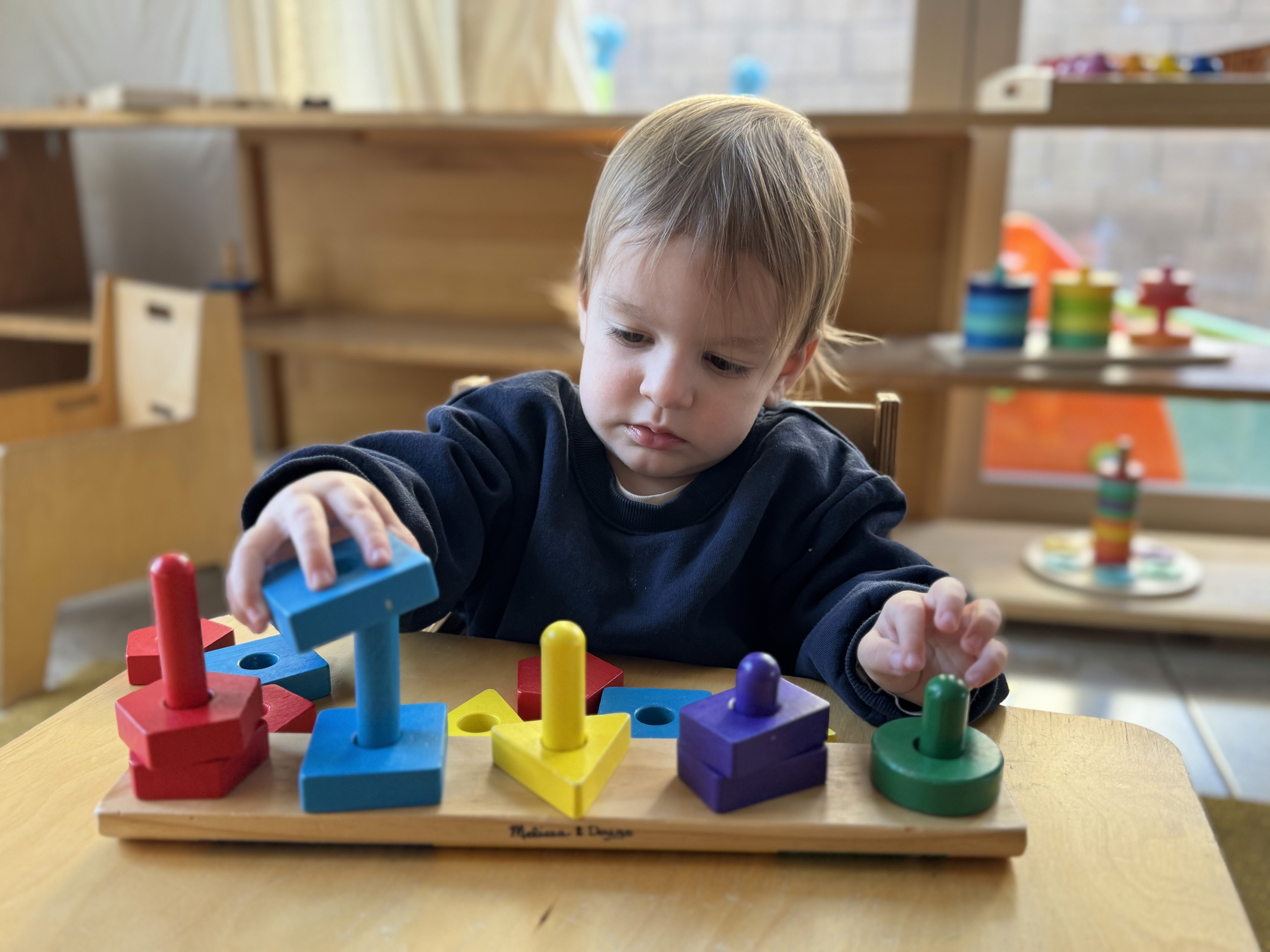 Toddler working with Montessori wooden shape sorting puzzle in infant classroom in Irvine CA