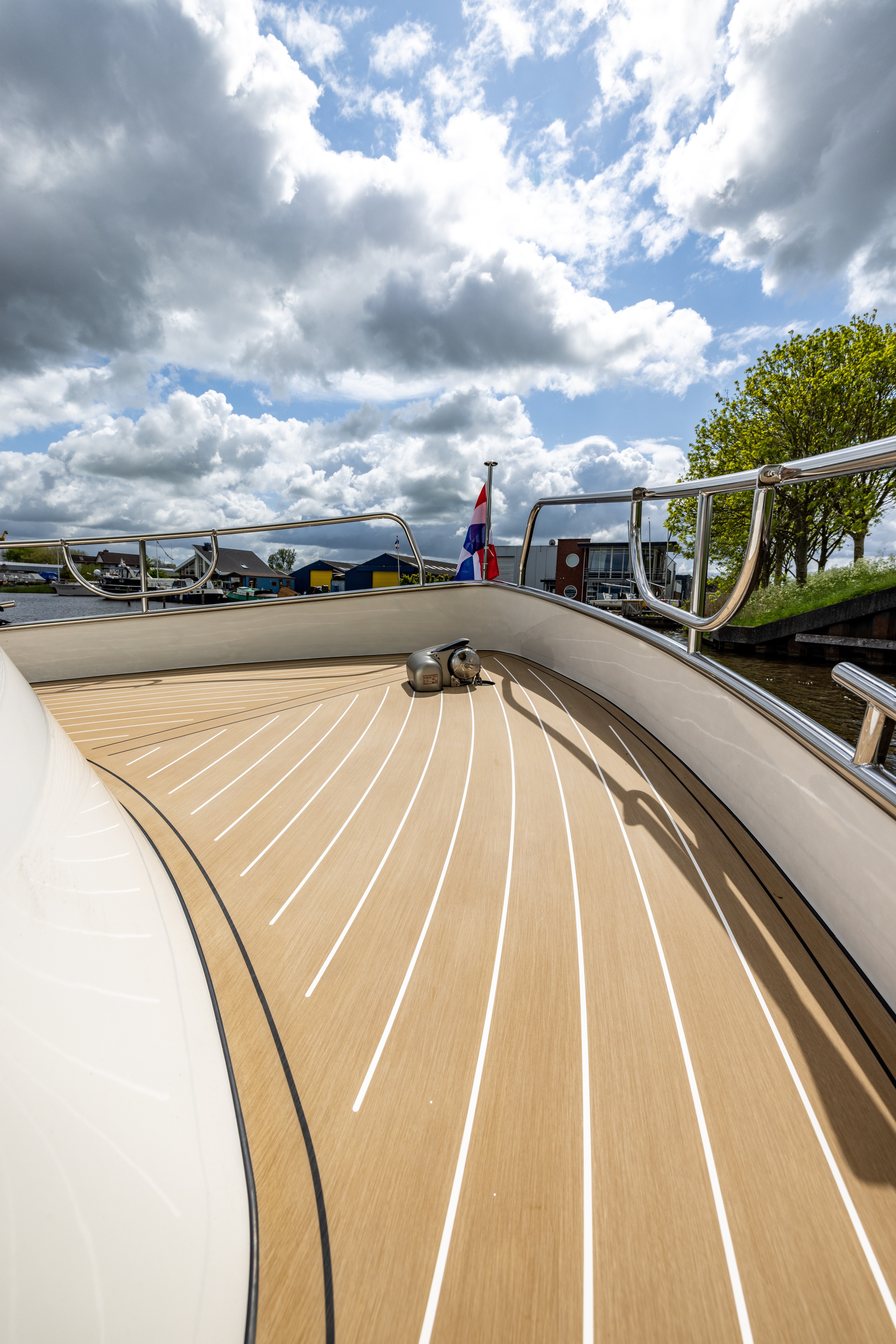 Wide-angle perspective view along a motor yacht foredeck fully covered in EcoDeck light oak composite decking, highlighting the product's ability to follow the curved hull shape with radiating plank patterns that taper elegantly toward the bow