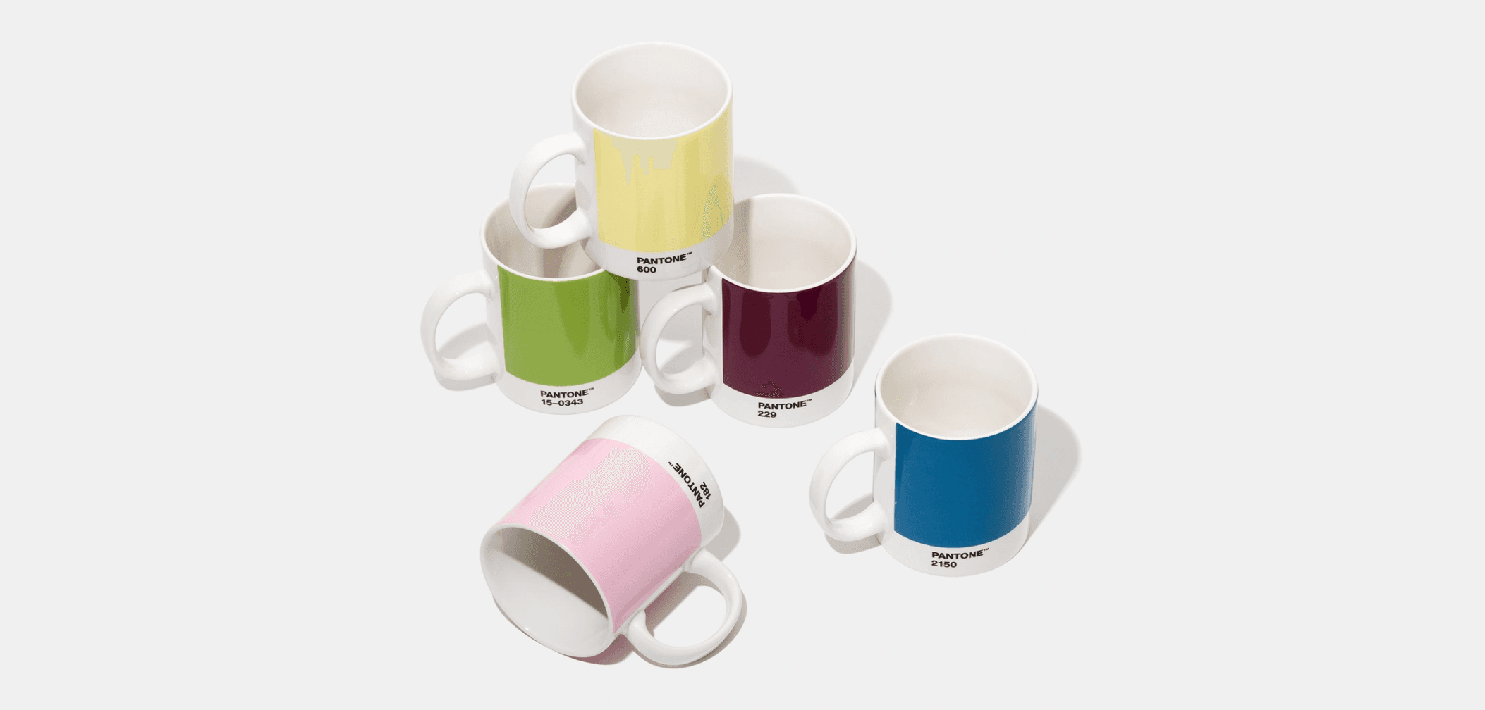 Set of colorful Pantone mugs in yellow, green, pink, burgundy, and blue arranged on a light surface.