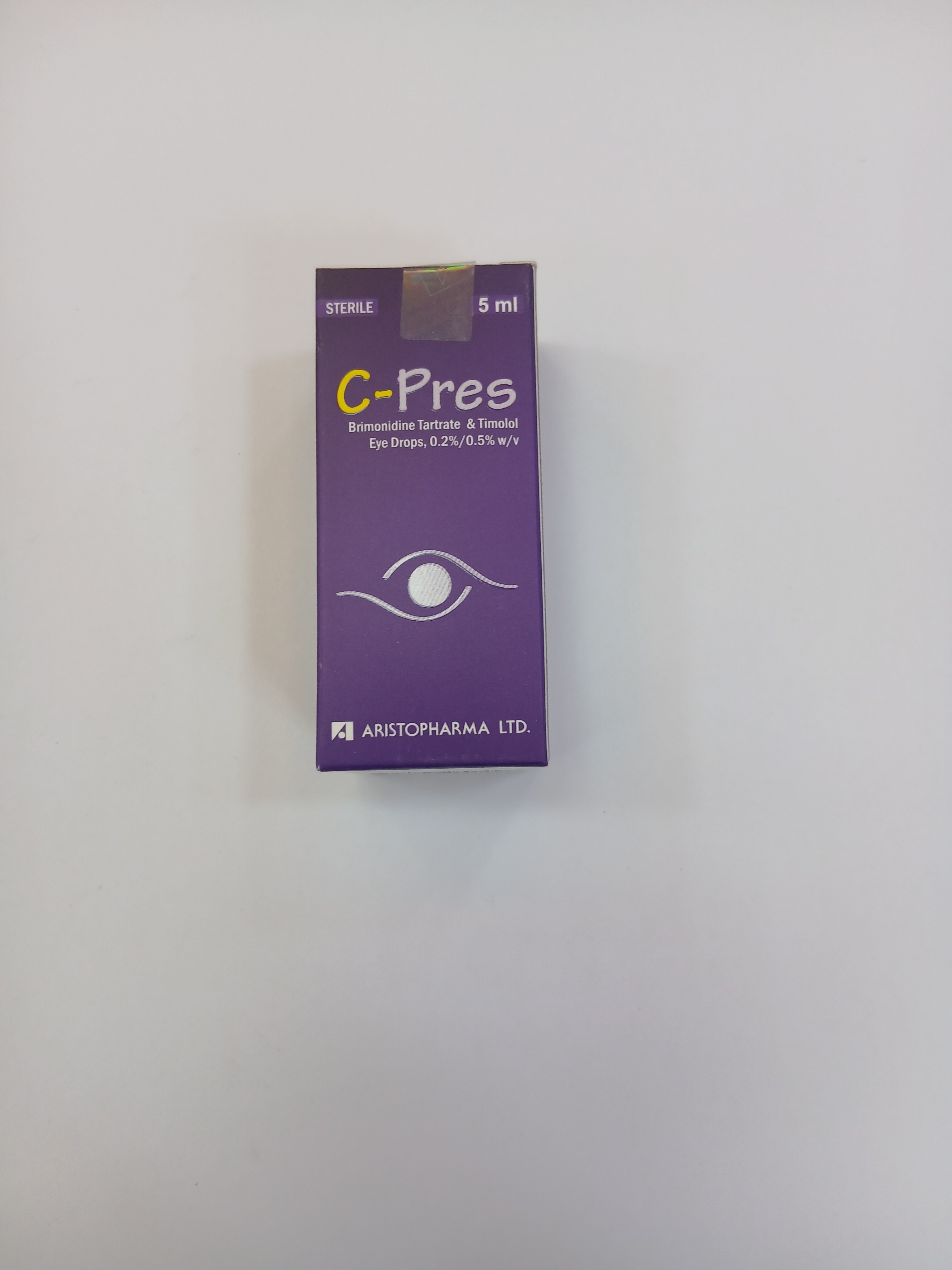 A small purple cardboard box packaging with a white label and eye graphic stands upright against a plain background, displaying a 5 milliliter drop bottle inside.