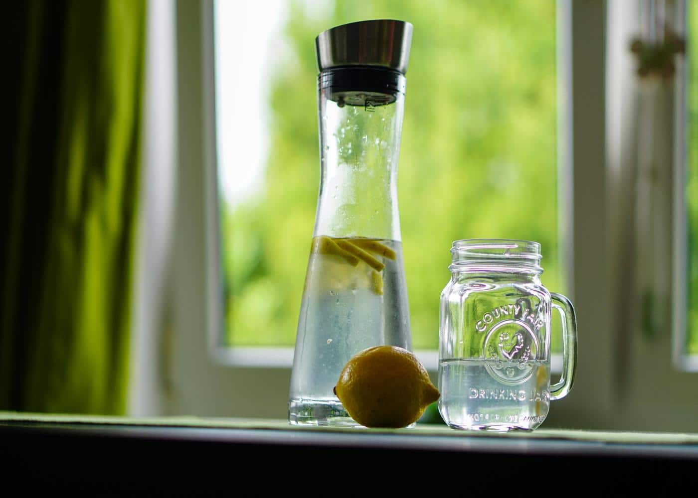 Lemon sitting next to a water pitcher and a mason jar with water