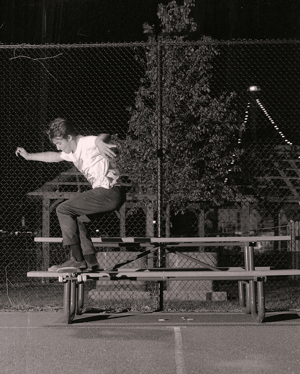 35mm film shot of a skateboarder tailsliding a bench, lit agressively from a speed flash out of frame.