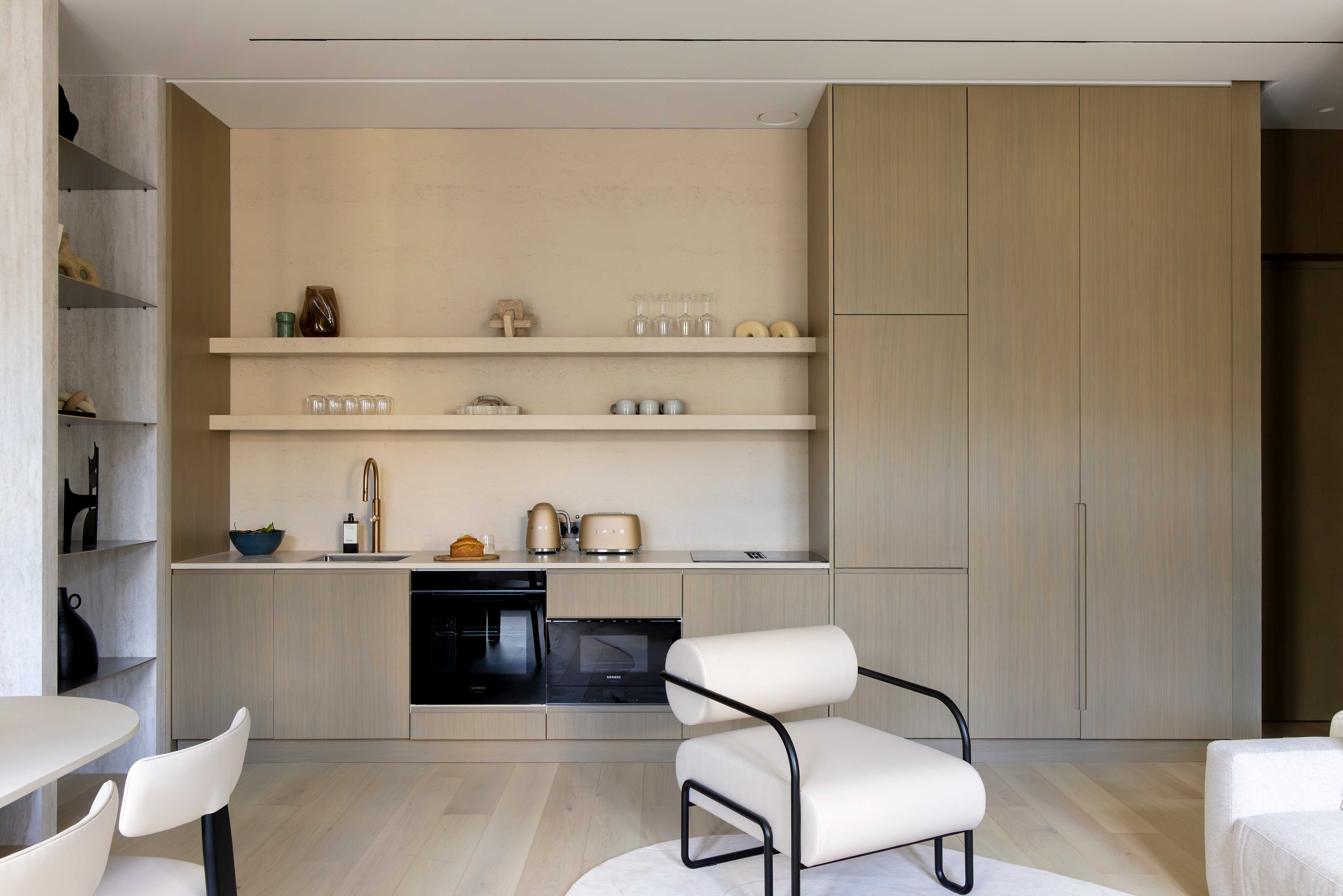 Vue frontale de la cuisine equipee en bois clair avec etageres ouvertes, fauteuil design blanc et parquet