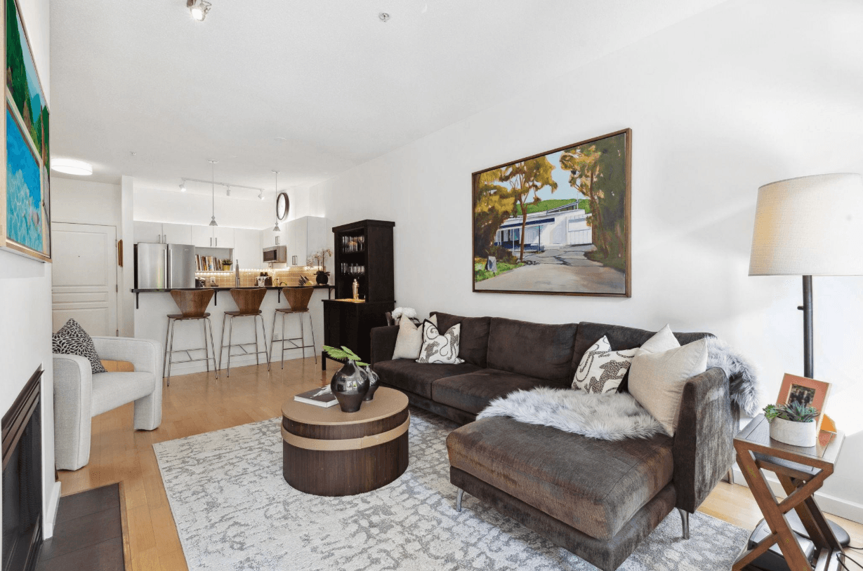 A cozy living room featuring a leather sofa, a coffee table, and wall art, with a glimpse of the kitchen area.