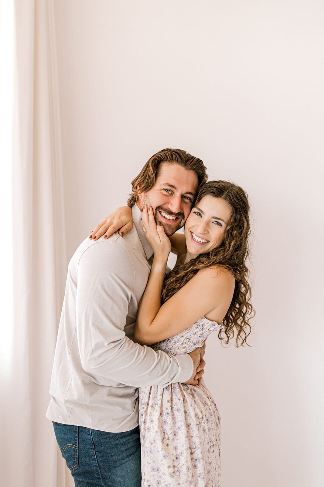 The couple laughs while embracing next to a window, bathed in natural light at Revelator Studio in Shreveport.