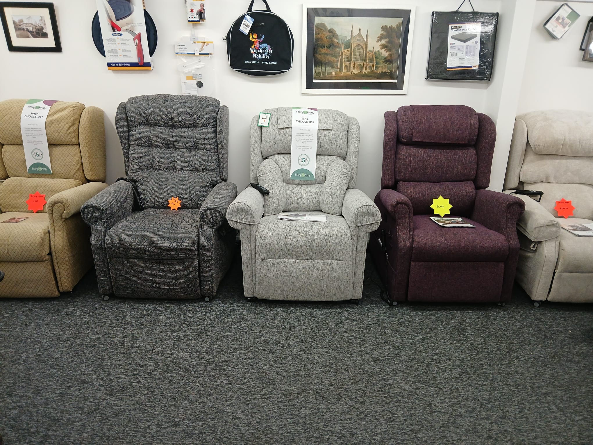 image shows a row of rise and recline armchairs. They are cream, grey, light grey, maroon and beige. Above them is a selection of paintings and a mobility scooter bag hanging on the wall.