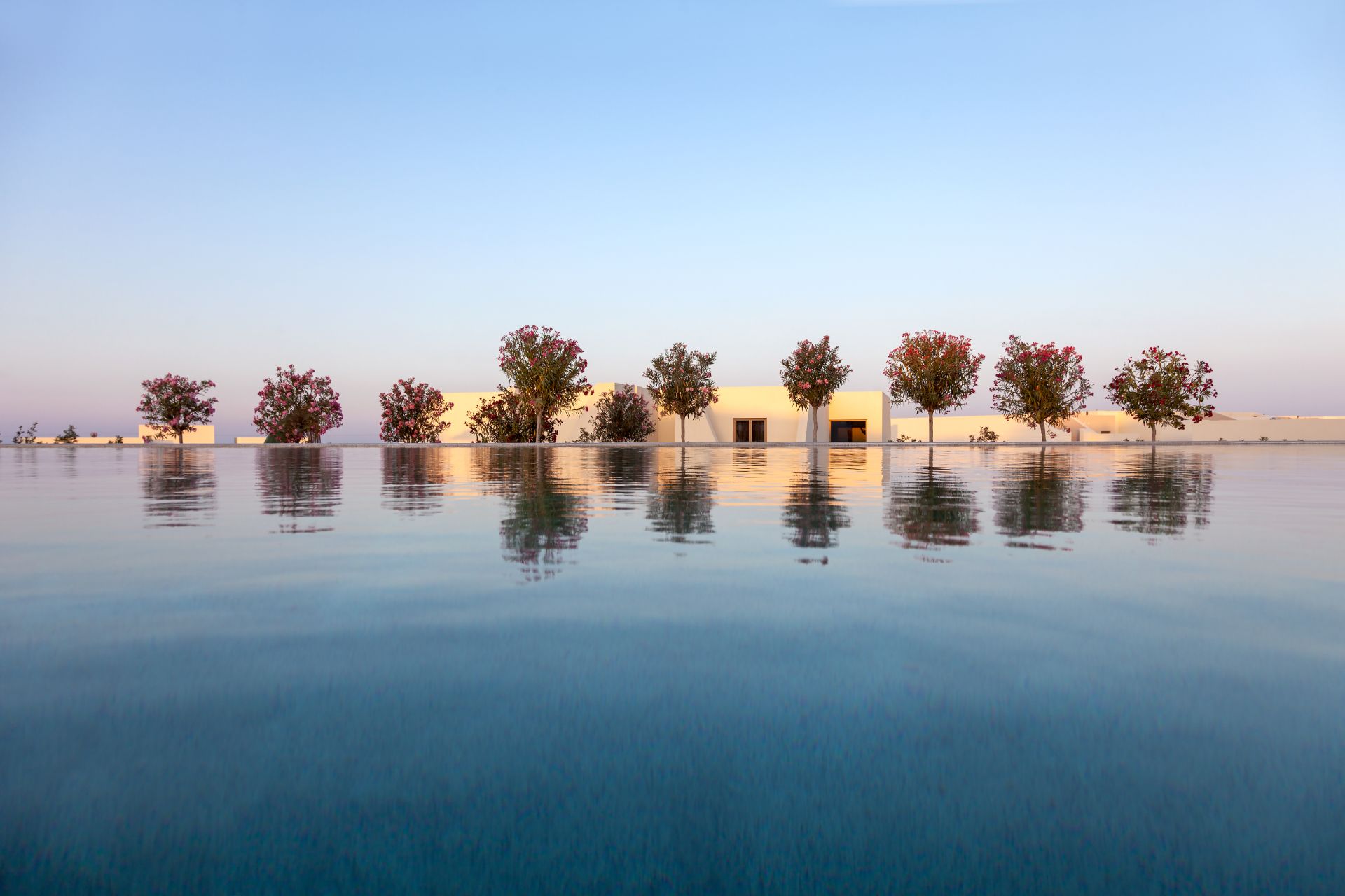 Landschaftsfoto mit Wasserspiegelung, Bäumen und einem weißen Gebäude unter blauem Himmel.