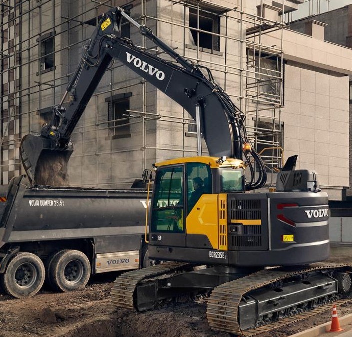 A person wearing a beige sweater and pants, with sunglasses, leans against a sunlit wall. The scene conveys a calm and relaxed atmosphere.