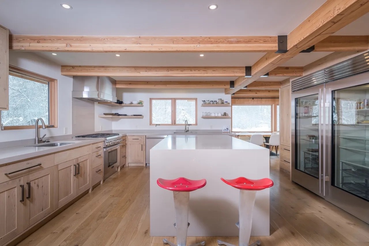 Bright white kitchen with a wood-beam ceiling and two red stools at the island