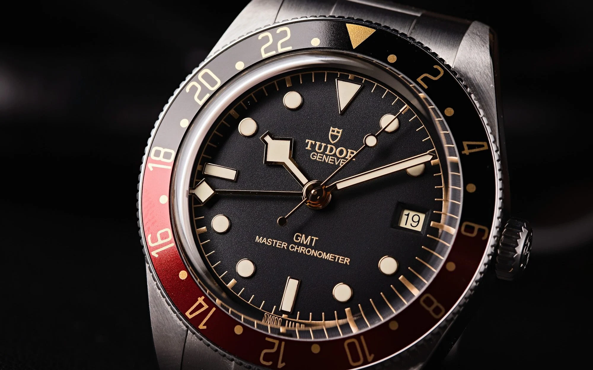 Tudor GMT Master Chronometer watch. Black dial, red bezel, and stainless steel band. Timepiece close-up.