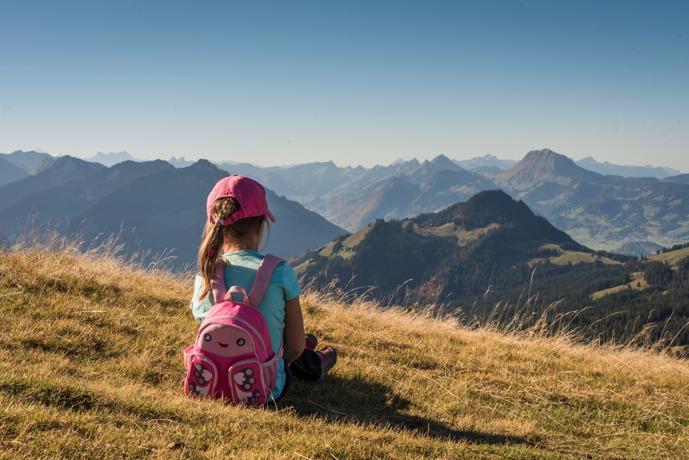 child sitting on a hill looking at the mountains