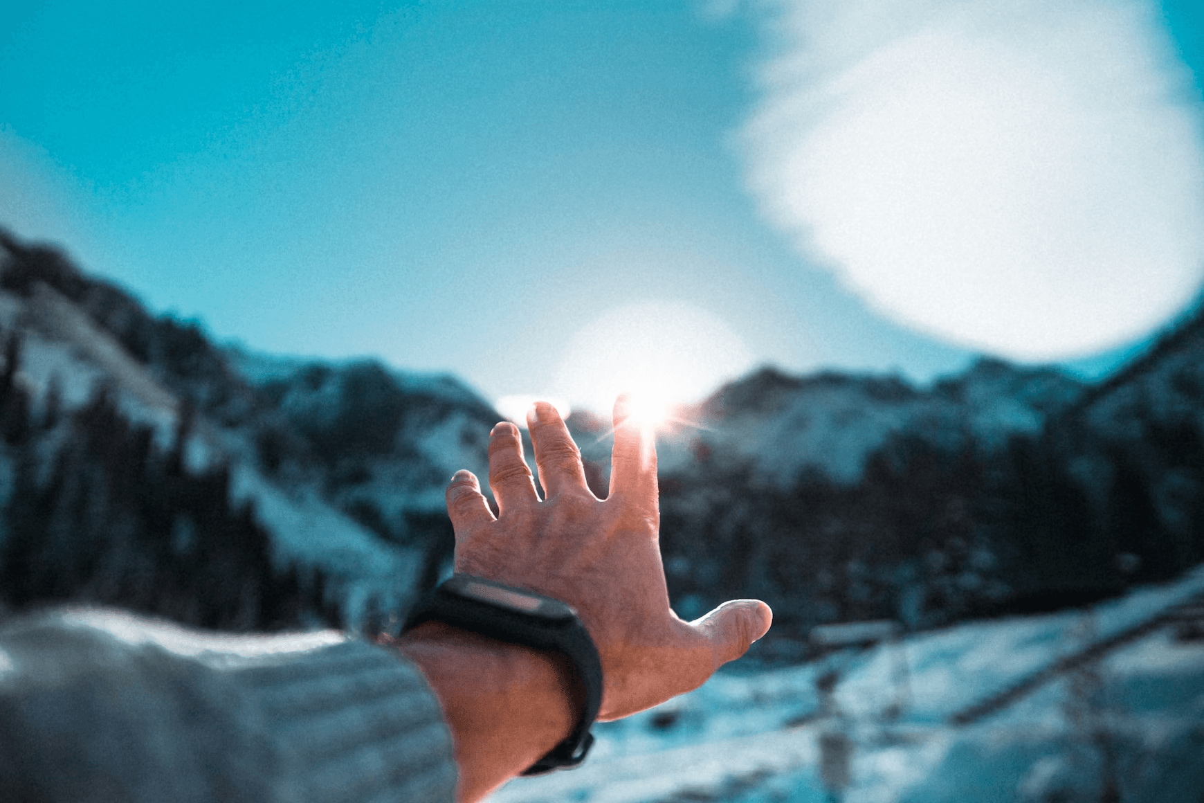A person's left hand pointing at a mountain sunrise