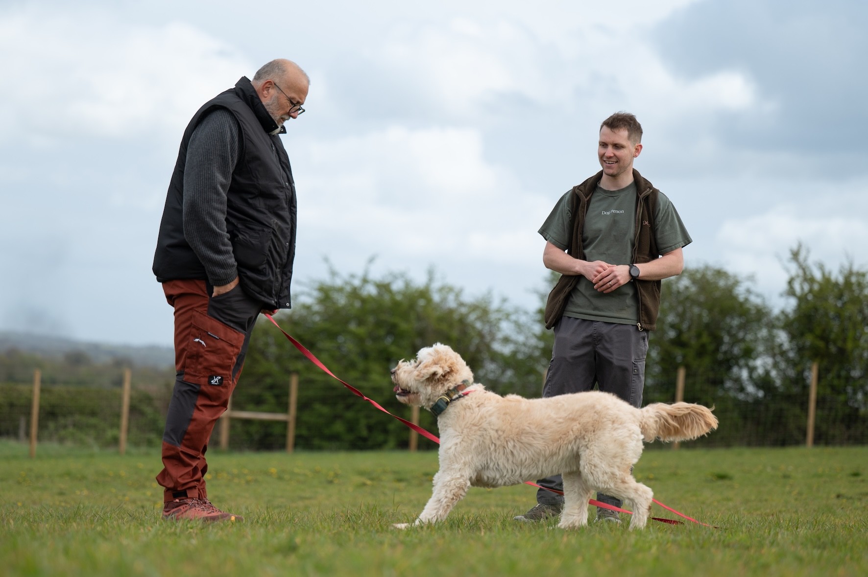 A dog on a long line running towards their owner, with a dog trainer beside them giving tips and advice