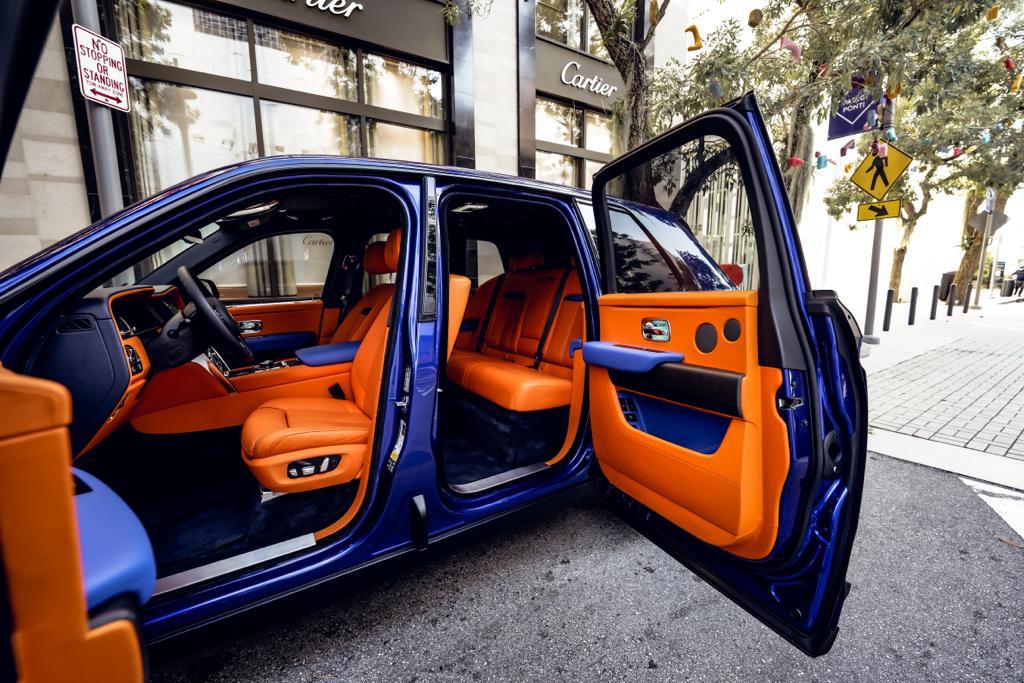 Interior view of Rolls-Royce Cullinan's open coach doors showing orange leather seats, door panels, and premium interior craftsmanship