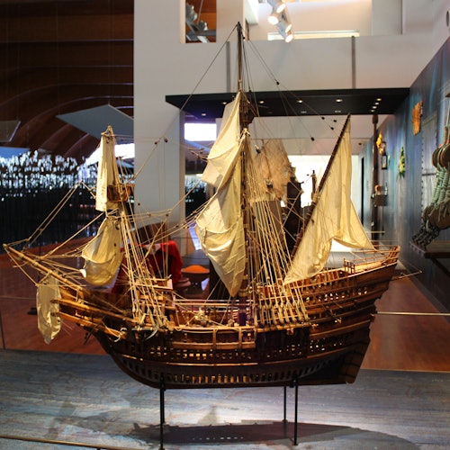 一艘詳細的木製船模型，配有白色帆，在明亮的博物館展示空間內展出。