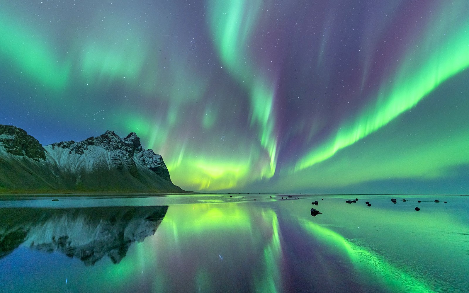 Northern Lights over a mountain reflected in a calm lake during a minibus tour.