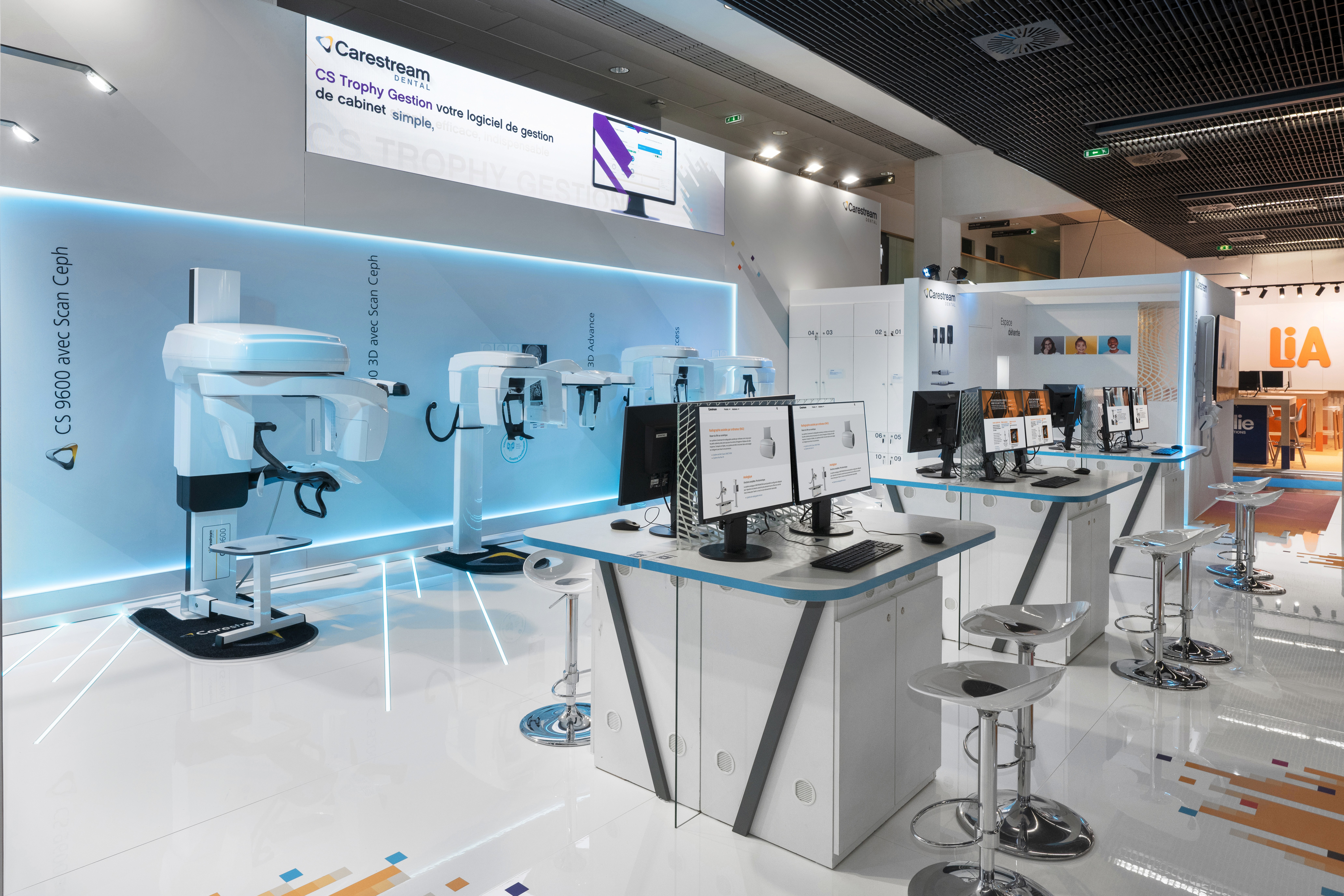 Stand Carestream Dental congrès ADF réalisé par Expace – vue intérieure avec mur d'imagerie dentaire rétroéclairé bleu, gamme CS 9600 Scan Ceph et postes de démonstration logiciel CS Trophy Gestion
