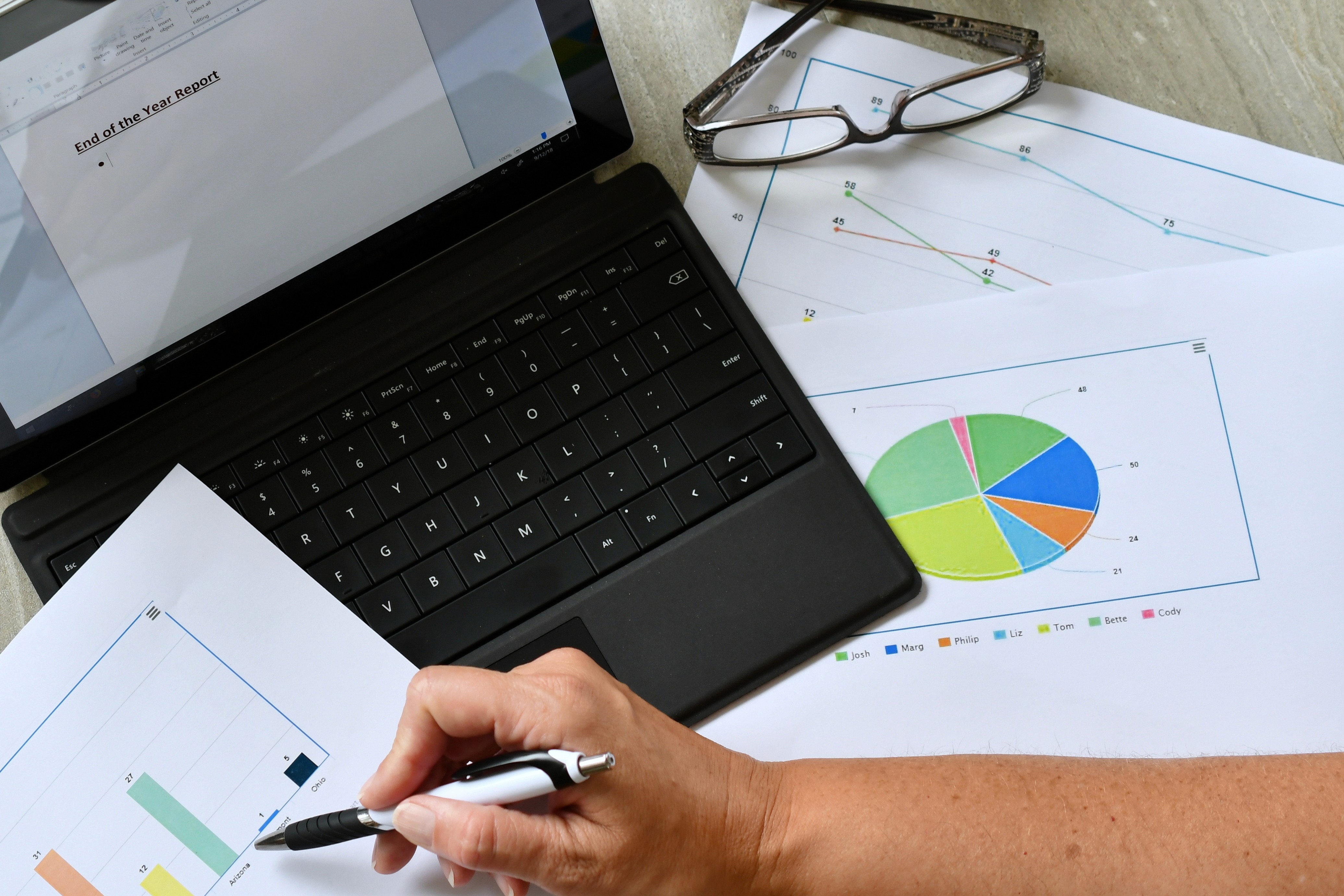 Person analyzing business charts and graphs while preparing an end-of-year report on a laptop with data sheets and pie chart visuals