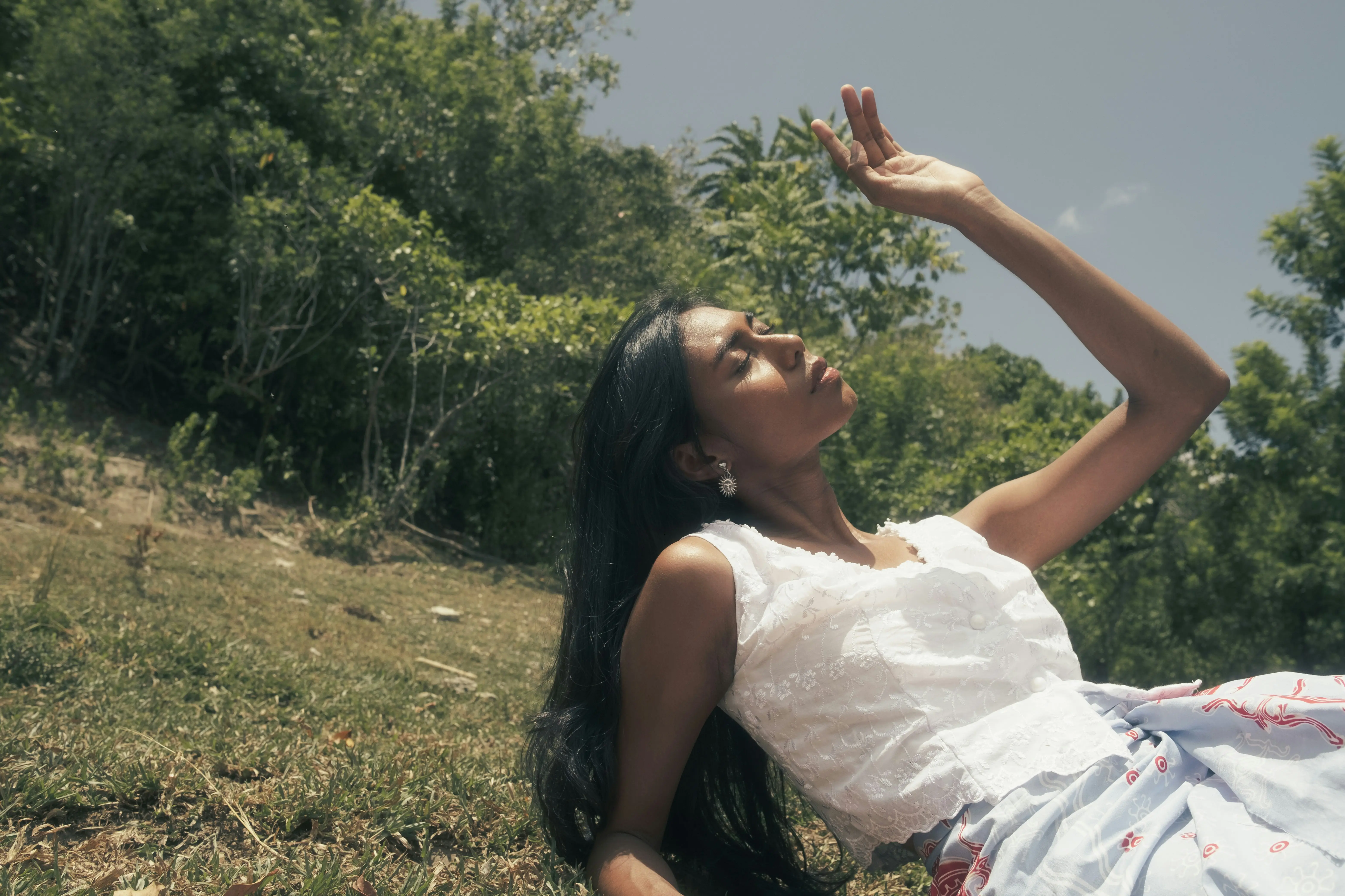 Woman wearing white laying on the grass, facing the sun.