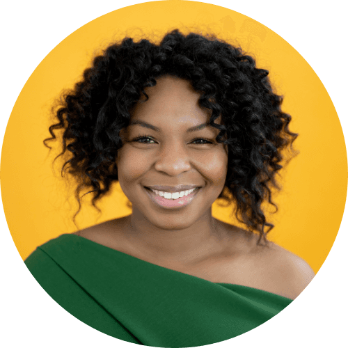 Portrait of a smiling woman with curly black hair, wearing a green top, with a yellow background.