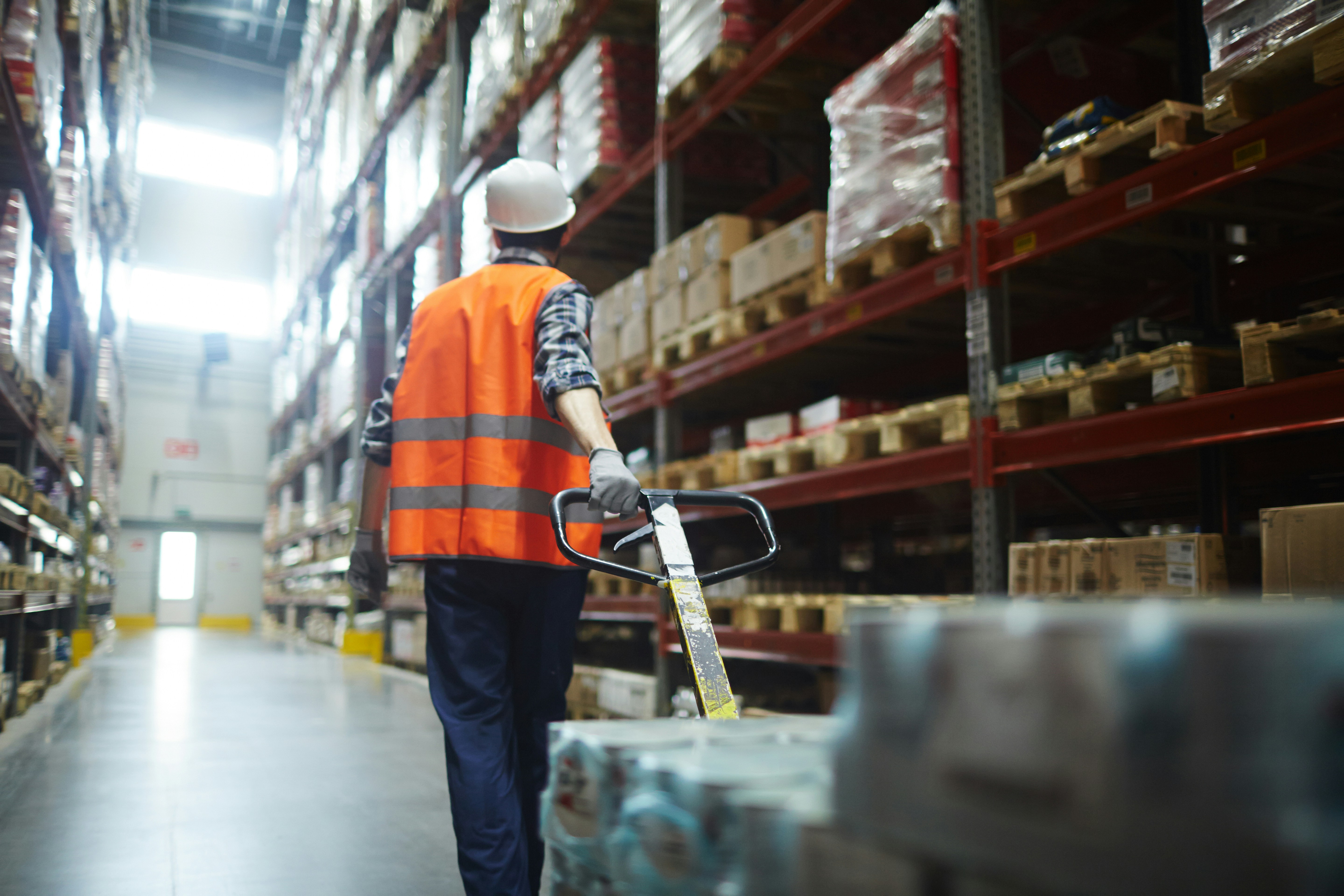 man walking down warehouse aisle with pallet truck