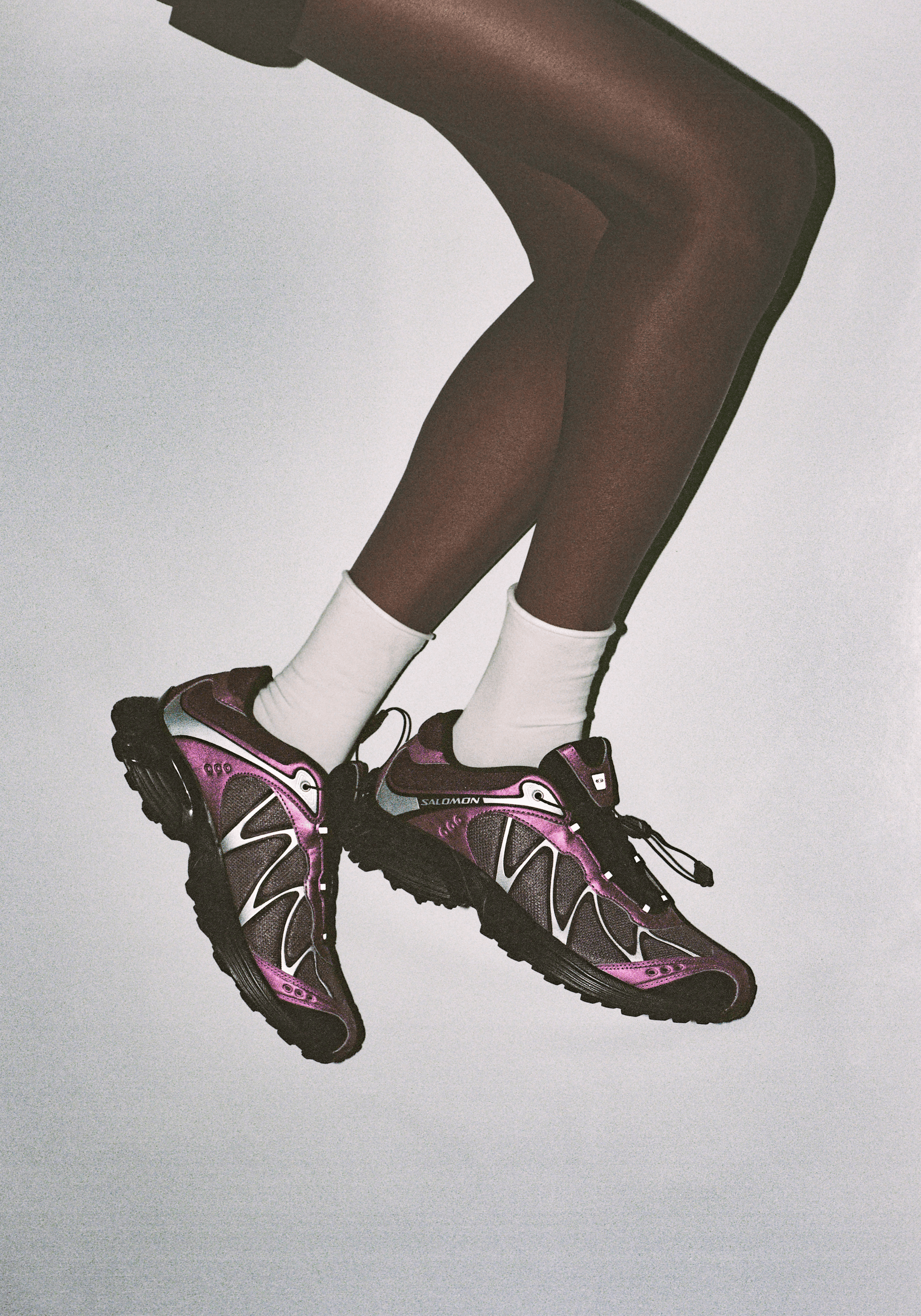Des jambes sur fond blanc portant une paire de baskets Salomon noires et roses