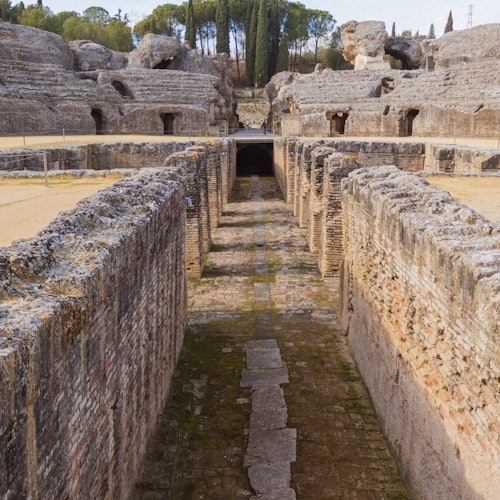 배경에 바위 지형과 나무로 둘러싸인, 돌담과 산책로가 있는 고대 유적지입니다.