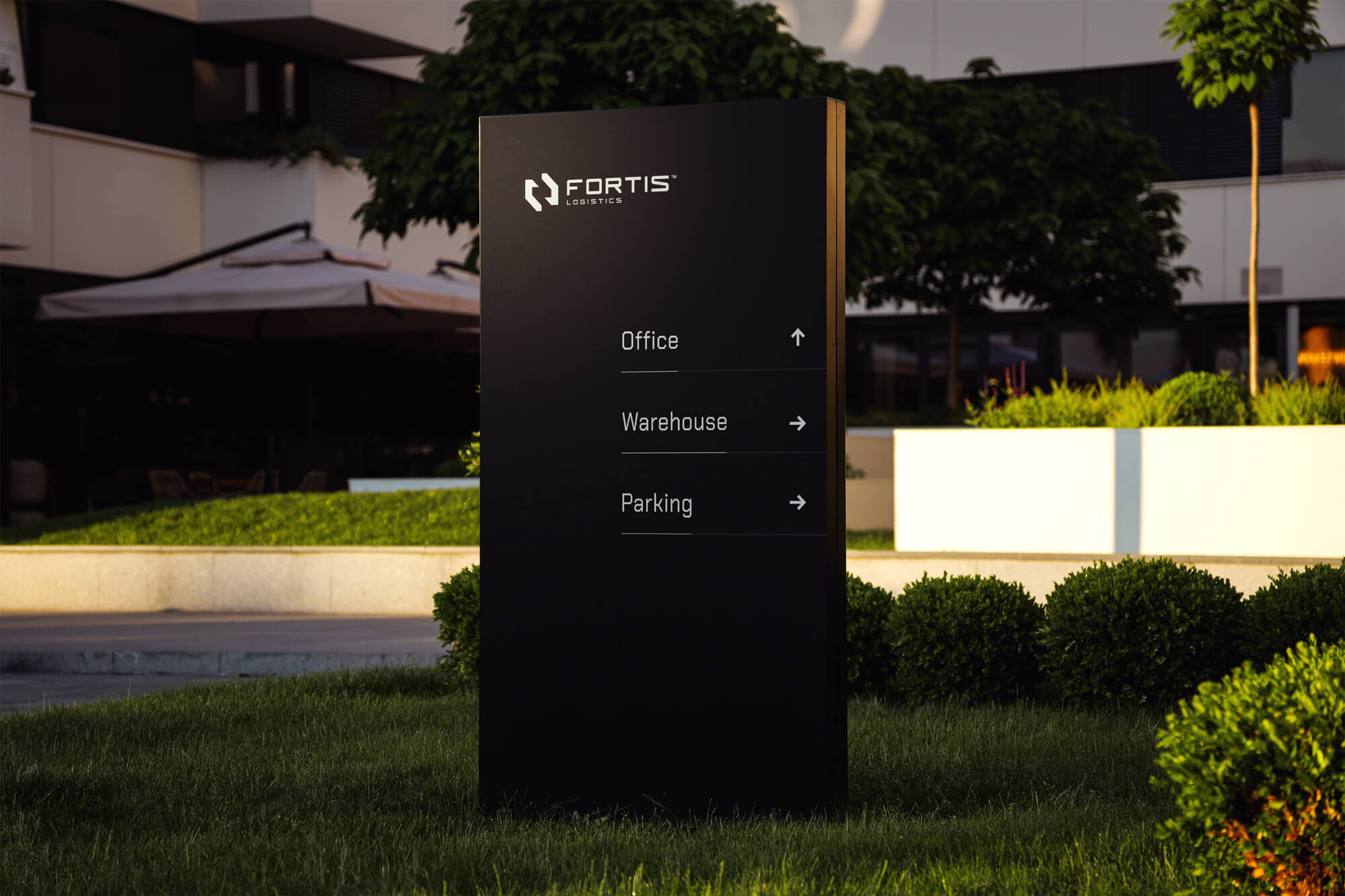 Modern black business sign featuring the white Fortis Logistics logo mounted on a rustic brick wall