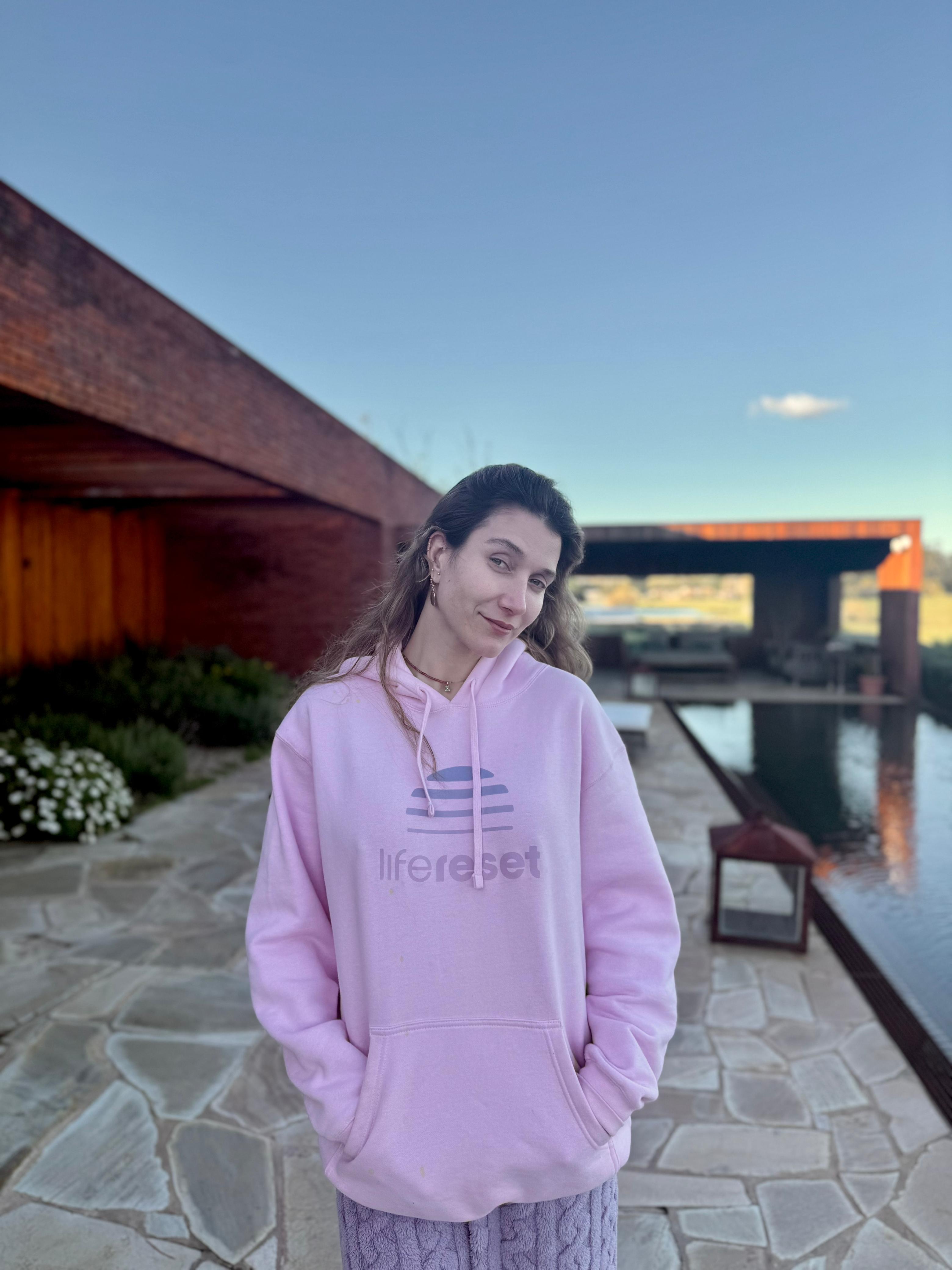 Smiling female therapist with short gray hair, wearing a brown top and a purple shawl, surrounded by a cozy background.