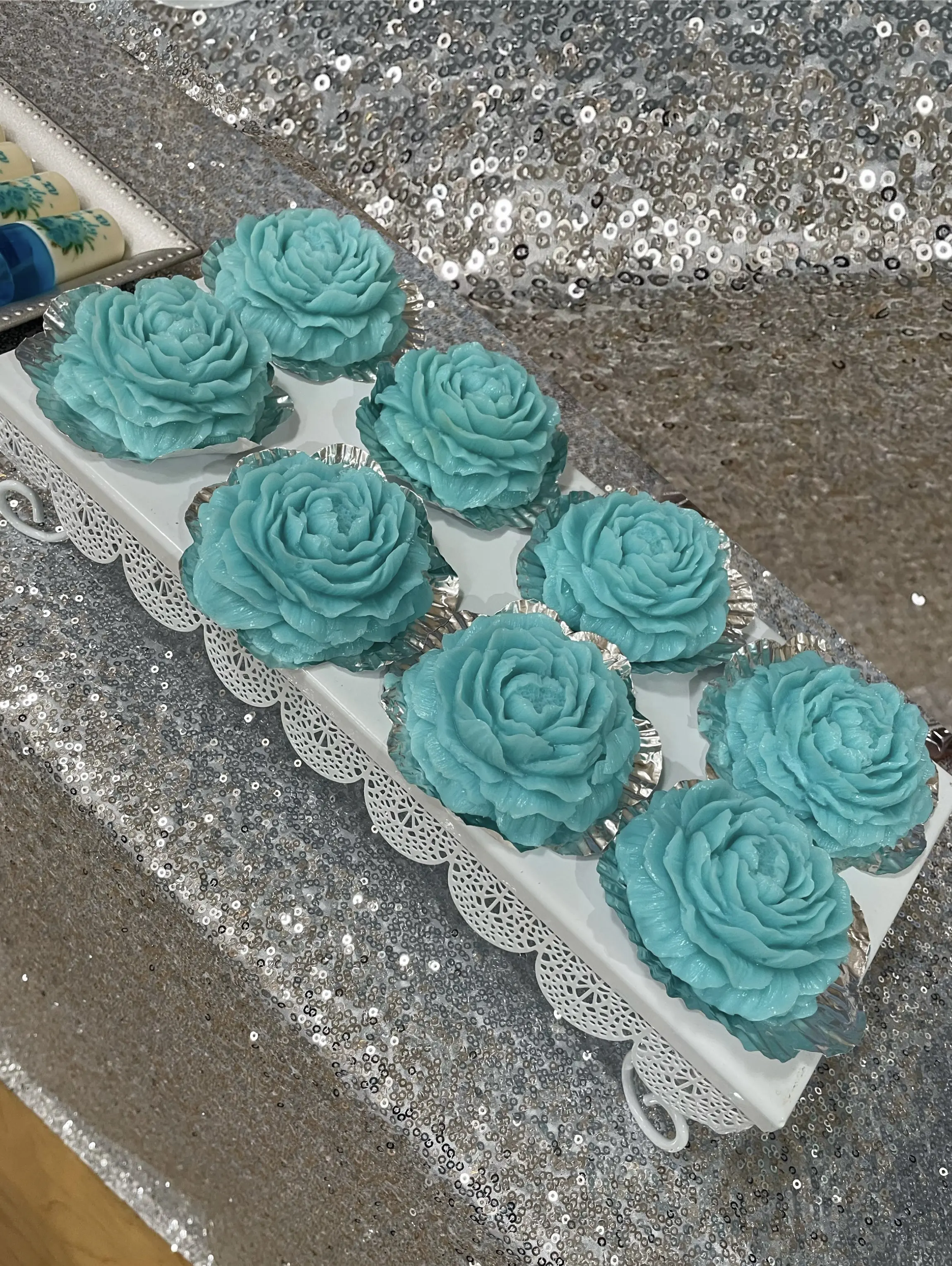 Rose-shaped gelatin desserts in a delicate blue hue, arranged elegantly on a white tray. Each piece is crafted to mimic a blooming rose, adding a touch of elegance to any dessert table. Susa’s Sweets & Balloons.